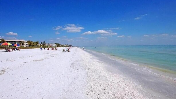 Ein Strand mit weißem Sand, klarem, blauem Wasser und einigen Sonnenschirmen.