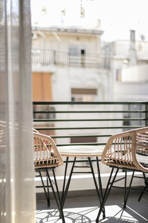Un balcone con sedie in vimini e un tavolo, con vista su un edificio con balconi.