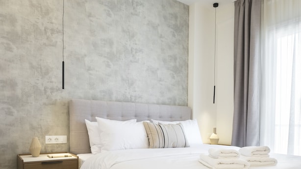 Een moderne slaapkamer met een groot bed, een nachtkastje, een lamp en uitzicht op de natuur door een raam met gordijnen.