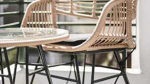 Een balkon met rieten stoelen en een glazen tafel.