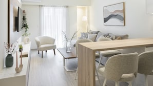 Een moderne, goed verlichte woonkamer met een houten eettafel, comfortabele zithoek en een groot raam met lichte gordijnen.