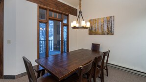 A dining room with a wooden table and chairs, a chandelier, a painting, and a view through a glass door. - Kayenta 7-Curate Telluride, Perfect SkI In/Out, Lift 4, Hot Tub, Fireplace (Mountain Village)