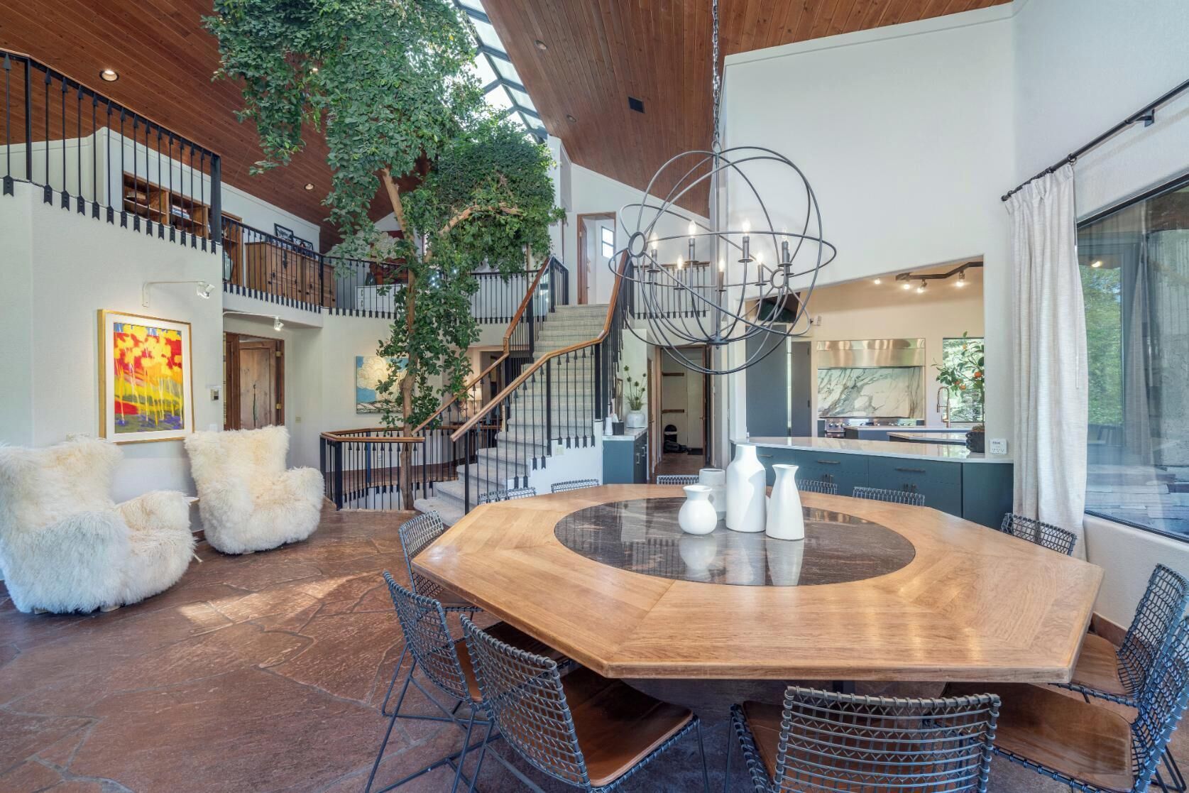 Un vaste espace dédié à la salle à manger, avec une grande table en bois entourée de chaises, et un escalier menant à un niveau supérieur.