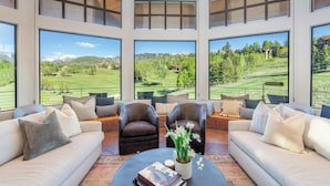 A modern living room with large windows, leather sofas, and a coffee table with books and a plant.