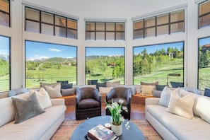 A modern living room with large windows, leather sofas, and a coffee table with books and a plant. - Singletree-Paragon by Curate Telluride-Pickleball, Pool Tbl, Hot Tub, Ping Pong (Mountain Village)