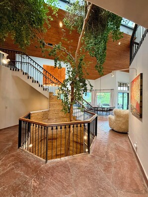 A spacious interior with a central staircase, a tree, and a dining area.