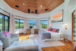 A spacious room with a wooden ceiling, large windows, a bed, a desk, and a sofa.