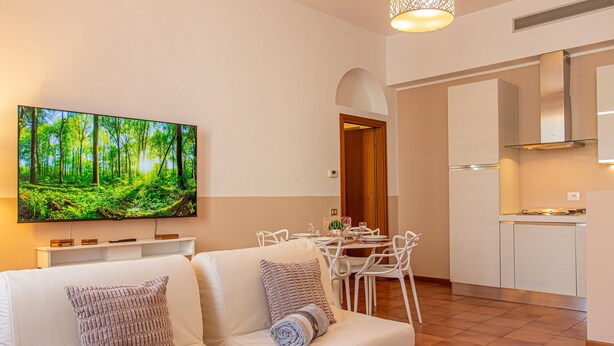 A modern living room with a flat-screen TV, white furniture, and a dining area with a table and chairs. - La Ringhiera Fiorita 201 Autodromof1 Villa Reale (Monza)