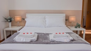 A neatly made bed with white linens, two bedside tables with lamps, and a small cactus on one table. - La Ringhiera Fiorita 201 Autodromof1 Villa Reale (Monza)