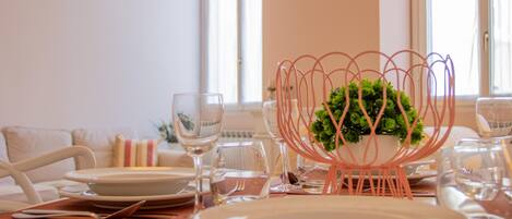 A dining table set with plates, glasses, and cutlery, with a decorative plant centerpiece.