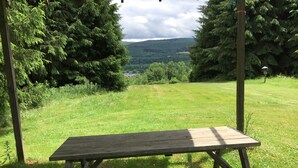 A picnic table in a grassy field with a view of a forest and hills in the background. - The Pines Hill Top. Bring your own tent. (Unadilla)