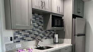 Une cuisine moderne avec des meubles gris, un réfrigérateur en acier inoxydable, un four à micro-ondes et un pare-feu en carreaux.