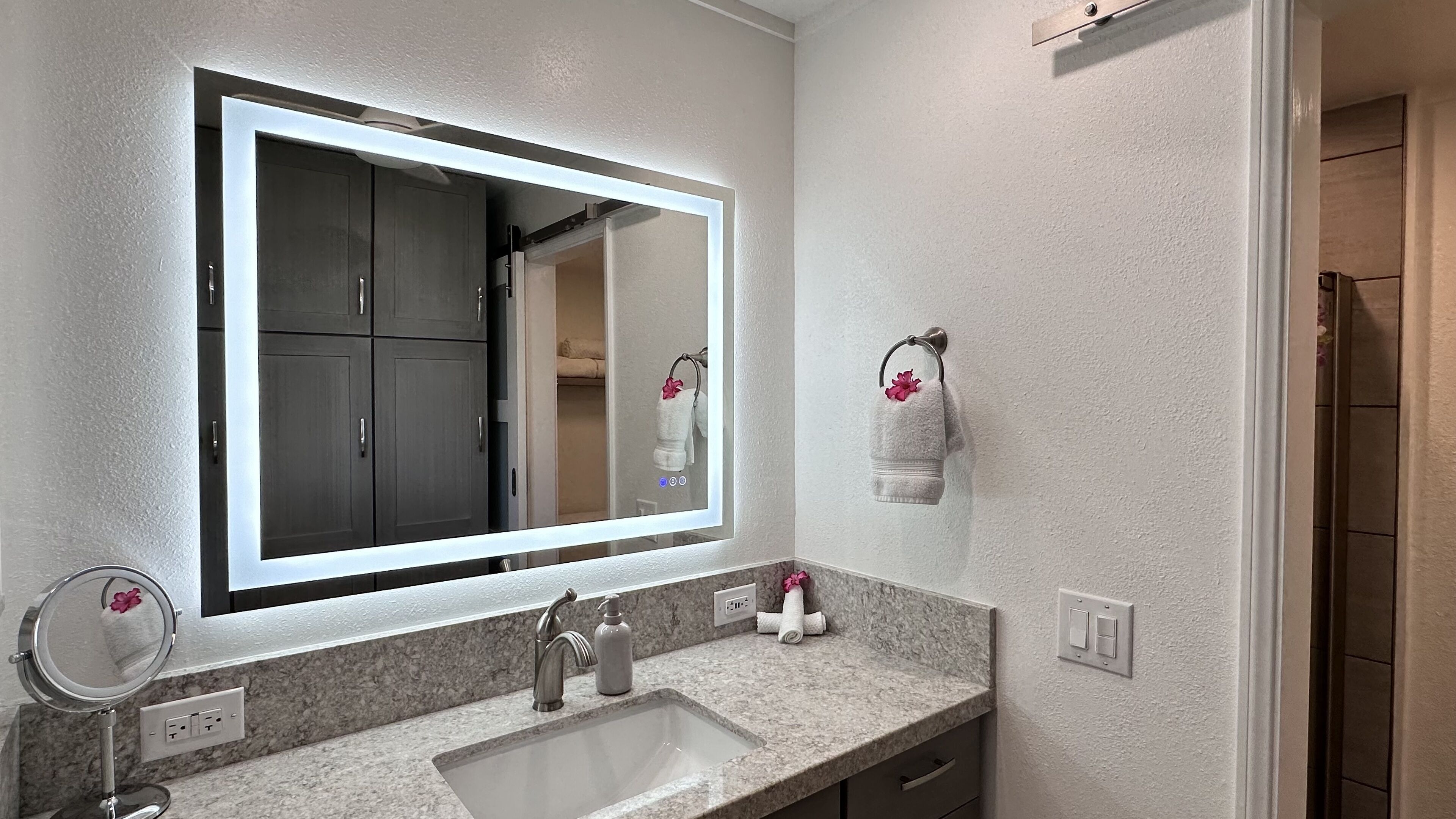 Un baño con un espejo grande, un lavamanos y un perchero para toallas.
