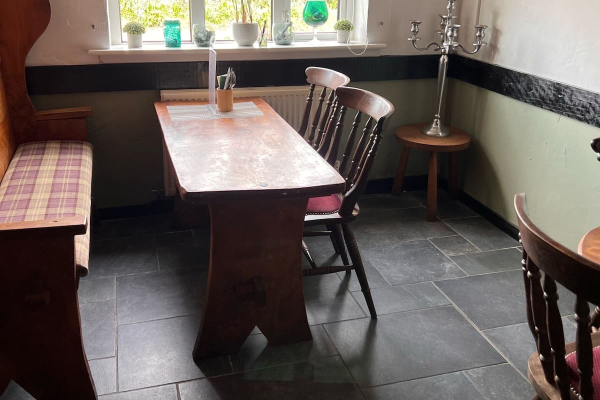 Un comedor con mesa y sillas de madera, una ventana con plantas y un muro blanco y negro.