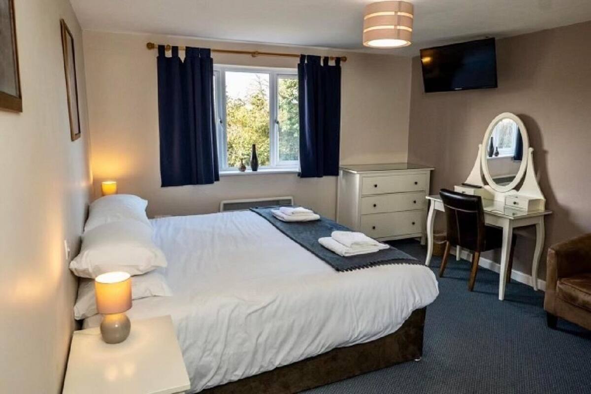 Una habitación de hotel con cama, lámpara de noche, cómoda, espejo y televisor en la pared.