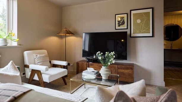 Una sala de estar moderna con un televisor de pantalla plana, un sillón blanco confortable, una mesa de centro de vidrio y un mueble de madera.
