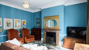 A living room with a blue wall, a fireplace, a television, and two brown armchairs. - The Fulham Town House - Spacious 4BDR House with Garden (London)