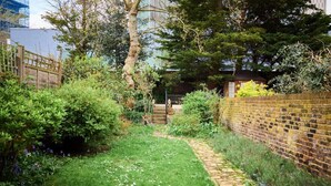 A garden pathway with a brick wall on one side and a wooden fence on the other, leading to a building with a dome-shaped roof. - The Fulham Town House - Spacious 4BDR House with Garden (London)