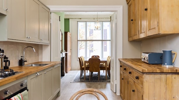 A kitchen with wooden cabinets, a sink, and a dining area with a table and chairs. - The Fulham Town House - Spacious 4BDR House with Garden (London)