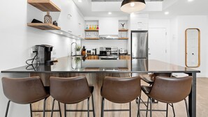 A modern kitchen with a central island, stainless steel appliances, wooden shelves, and bar stools. - Le Downtown (rooftop pool and gym) (Québec)