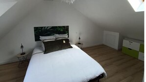 A bedroom with a sloped ceiling, a bed with white bedding, a green and white headboard, two bedside tables with lamps, and a radiator. - - L'olivier - (Dozulé)