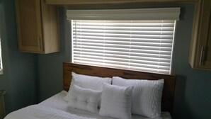 Ein Schlafzimmer mit einem Holzkopfende, weißer Bettwäsche und einem Fenster mit Jalousien.