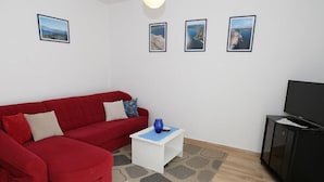 A living room with a red sofa, a small white table, and a black cabinet. There are three framed pictures on the wall.