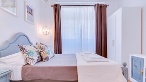 A neatly arranged bedroom with a bed, bedside tables, a nightstand, a chandelier, and a window with curtains.