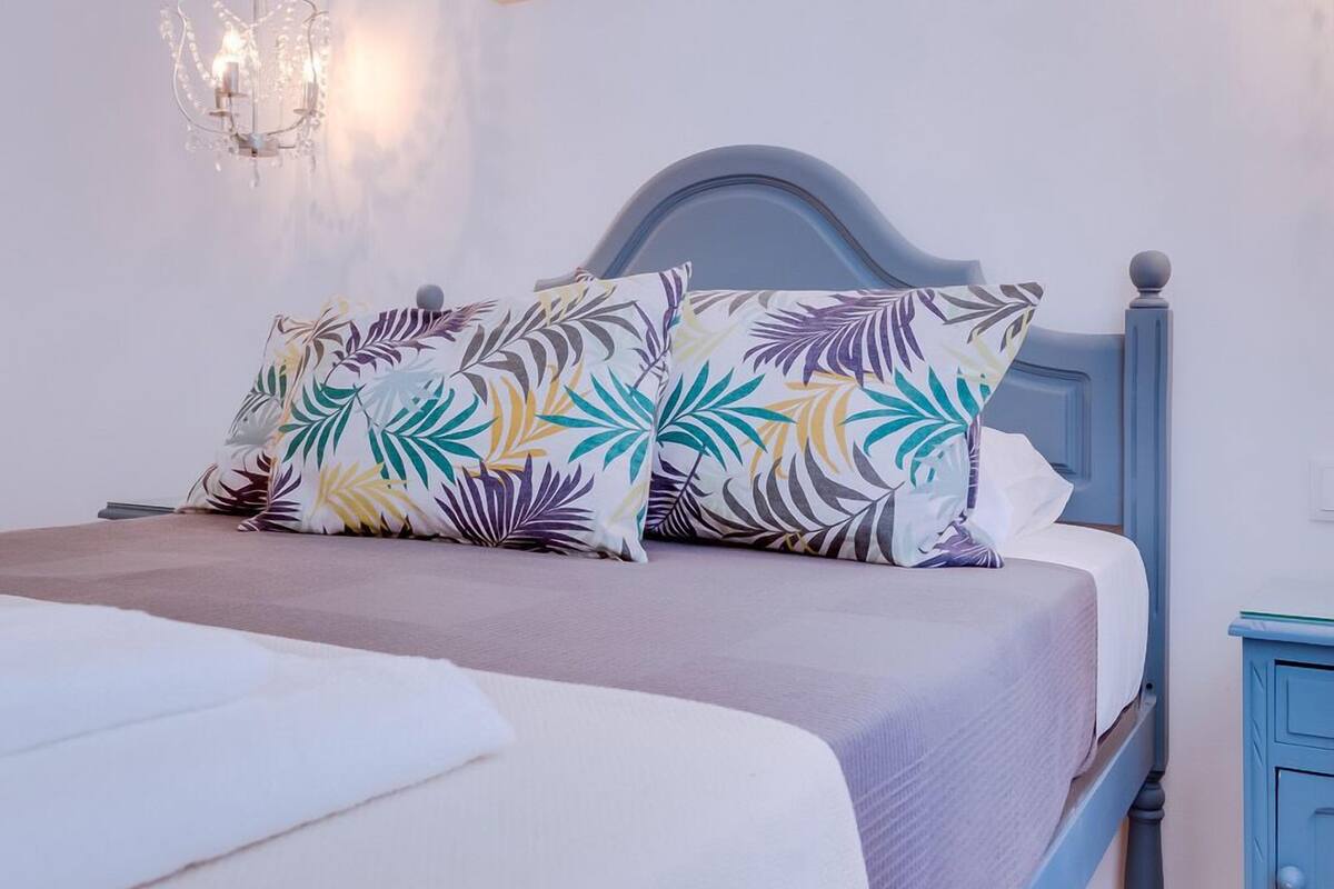 Quarto com cama, mesa de cabeceira, luminária na parede e duas fotos emolduradas.