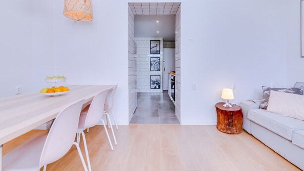A modern, well-lit living area with a dining table, chairs, a sofa, and a lamp.