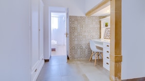 A hallway leading to a bathroom with patterned tiles, a white sink, and a chair.