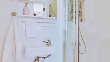 Un baño con cabina de ducha de vidrio, un lavabo blanco y un perchero para toallas.