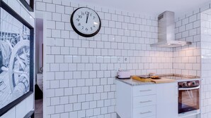 A modern kitchen with white tiled walls, a clock, a toaster, and a built-in oven.