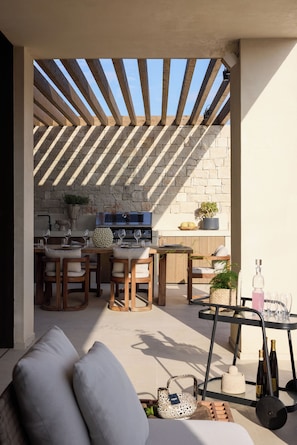 Eine Terrasse im Freien mit einer Steinmauer, Holzmöbeln und Grillbereich.