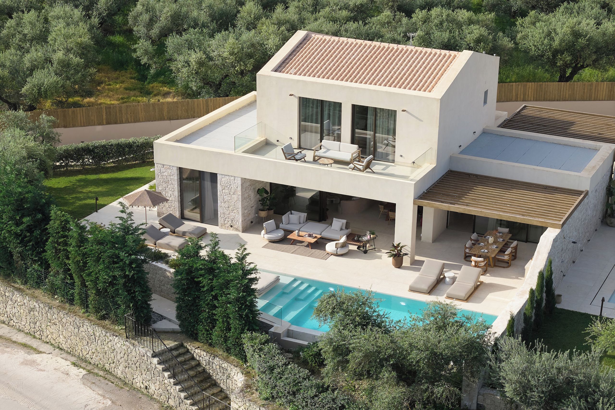 A modern two-story house with a swimming pool, outdoor seating, and a stone retaining wall.