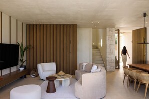 A modern living room with a flat-screen TV, sofas, a coffee table, and a dining area with a wooden table and chairs.