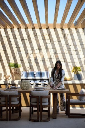 An outdoor patio with a stone wall, wooden furniture, and a grill.