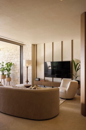 A modern living room with a large curved sofa, a flat-screen TV mounted on the wall, and a stone accent wall.