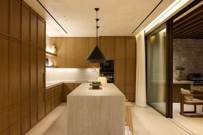 A modern kitchen with wooden cabinets, a central island, and a stone wall. - Valerozo Immensa Villa (Ionian Islands, Zakynthos)