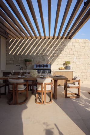 An outdoor patio with a stone wall, wooden furniture, and a built-in grill.