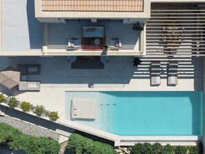 An aerial view of a modern pool area with lounge chairs, a sunbed, and a small table with a chair.