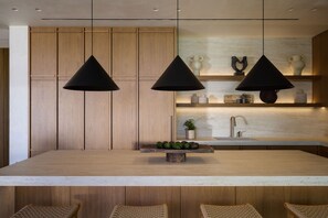 A modern kitchen with wooden cabinets, a central island, pendant lights, and a built-in sink.