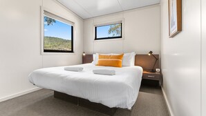Una habitación de hotel moderna con una cama grande, dos ventanas, una mesita de noche y un cuadro en la pared.