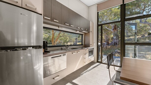 Una cocina moderna con electrodomésticos de acero inoxidable, un ventanal con vistas a árboles y una zona de comedor con una silla.