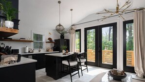 Une cuisine moderne dotée d’un îlot central, de meubles de rangement noirs et d’une grande fenêtre donnant sur une terrasse en bois.