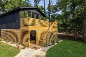 A modern wooden cabin with a black exterior, a wooden staircase, and a small door.