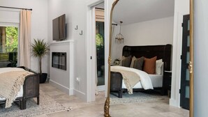 Une chambre avec un grand miroir, un lit avec de nombreux oreillers, une télévision et une plante en pot.