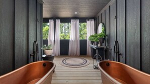 Une terrasse en bois avec deux baignoires en bois, un tapis rond et des plantes en pot.