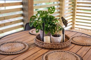A round wooden table with woven placemats, two potted plants, and candles.