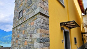 Un edificio de piedra con fachada amarilla, una terraza de madera y vistas a un lago.